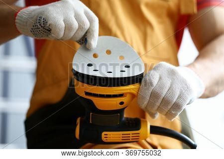 Close-up Of Carpenter Worker Changing Disc On Yellow Sander Machine. Construction Repairman In White