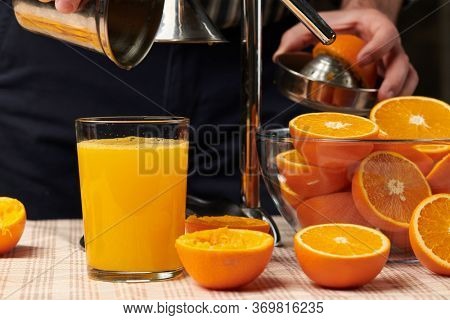 Squeezing an orange with a manual press, close view, making a glass of fresh. Fresh oranges on a wooden table, whole, squeezed and sliced.