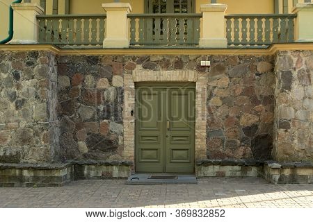 Green Olive Wooden Door In A Stone Wall. The Second Floor Is Visible With Carved Wooden Balconies. E