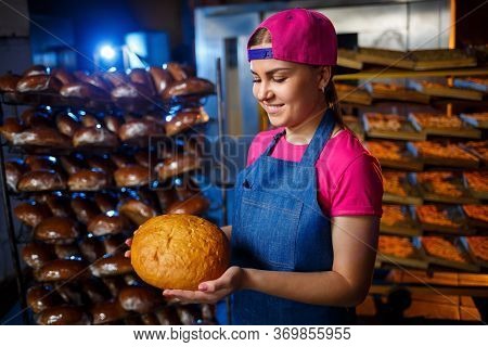 The Stage Of Baking In A Bakery. Portrait Of A Baker Girl With Bread In Her Hands Against The Backgr