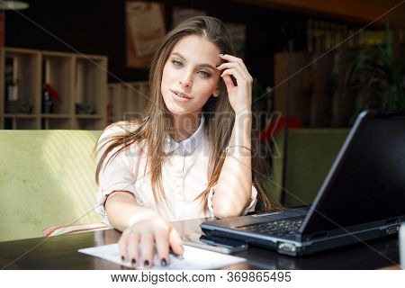 Beautiful Girl At A Table In A Cafe Is Sitting In Front Of A Laptop.