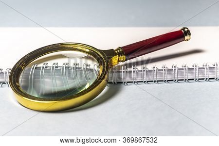Close Up Golden Magnifying Glass Loupe With Red Wooden Handle On White Planner Or Notebook And Gray 