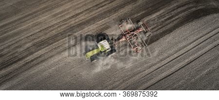 Aerial View Of A Clean Field In Which The Tractor Makes Vertical Tillage. Red Tillage Equipment And 