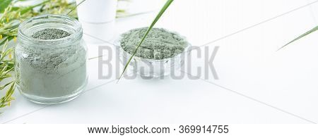 Glass Jar With Green Clay, Ingredients Of A Cleansing Facial Mask On A White Background. Spa And Bod