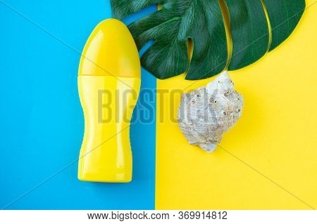 Yellow Bottle With Skin Care Product, Seashell And Green Leaf Of Monstera On Yellow And Blue Backgro