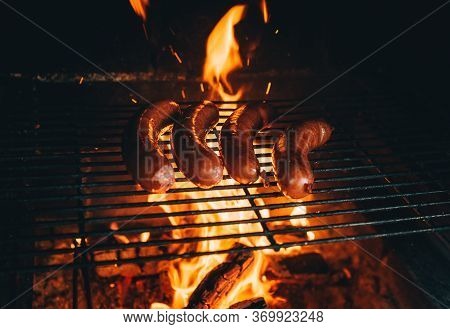 Cooking A Sausages Meat On Barbecue. Four Sausages On Grill. Concept Of Eating Outdoor At Country Ho