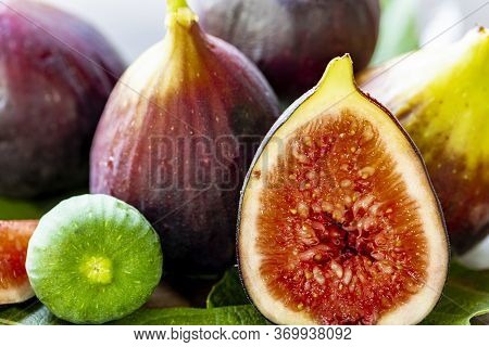 Close Up Of Figs On Top Of Green Leaves On Rustic Wooden Background
