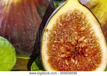 Close Up Of Figs On Top Of Green Leaves On Rustic Wooden Background