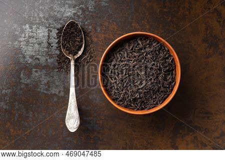 Dry Black Tea Leaves In A Clay Bowl And A Vintage Spoon On A Dark Background Top View. Large-leaf An