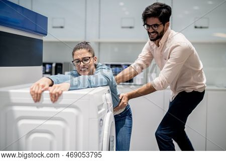 Man Taking Away Wife From Washing Machine. Whiteware Department Interior.