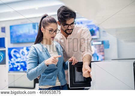 Young Caucasain Couple Looking For Good Quality Microwave While Standing In Tech Store.