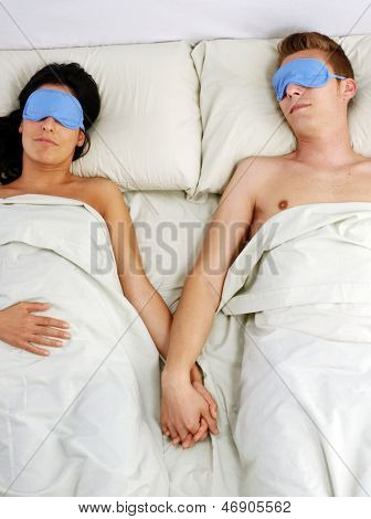 Jolie jeune couple endormi sur le lit à l'aide de masque pour les yeux.
