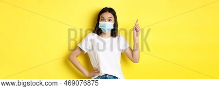 Covid, Health Care And Pandemic Concept. Asian Female Model In Medical Mask And White T-shirt Pointi