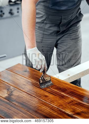 Man Paints Wooden Boards With Paint Brush. Carpenter Cabinetmaker Varnishes Wooden Surface. Authenti
