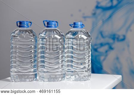 Three Full 5 Liter Bottles Of Water On A White Table On A Gray Background. Water Delivery