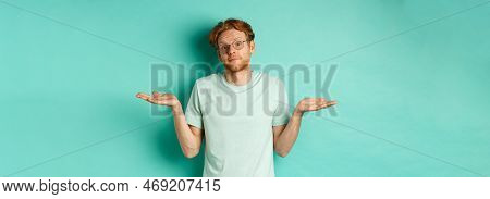 Portrait Of Confused Redhead Man In T-shirt And Glasses Know Nothing, Shrugging Shoulders And Lookin