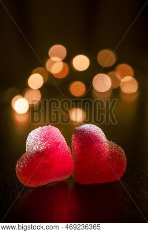 Two Red Sugar Marmalade Candies In Shape Of Heart On Black Background, Lit From Side, Behind Round Y