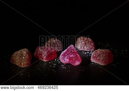 Six Red Sugar Marmalade Candies In The Shape Of A Heart On A Black Background, Lit From The Side, Wi