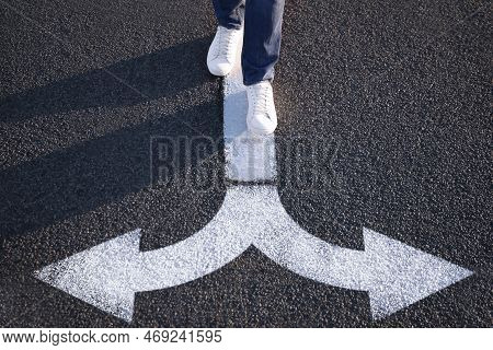 Choice Of Way. Man Walking Towards Drawn Marks On Road, Closeup. White Arrows Pointing In Opposite D