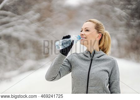 Sportswoman Drinking Water And Taking A Break While Standing In Nature At Snowy Winter Day. Healthy 