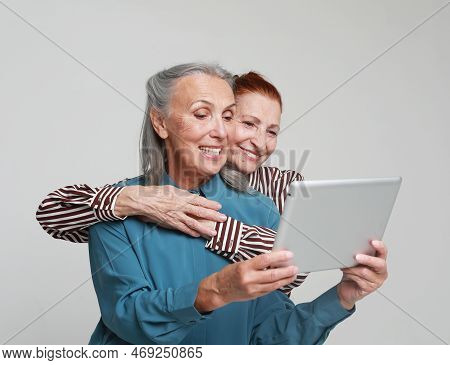 Two Mature Female Friends Looking Through Old Photos Digital Album Together With Tablet Device Over