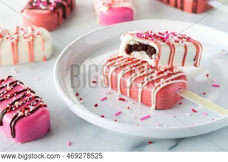 Valentines Day Cakesicles On A Plate With Sprinkles With A Bite Out Of One.