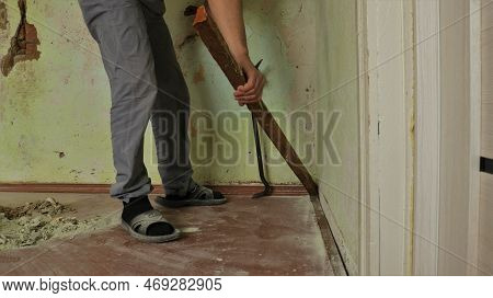 A Man Breaks A Wooden Floor Plinth With An Iron Crowbar In A Refurbished Room, Breaking Out An Old P