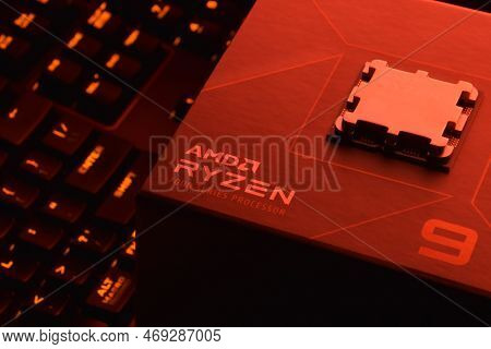A Close-up Of An Amd Ryzen 9 3900X Processor In A Packaging Box With Backlit Keyboards In The Backgr