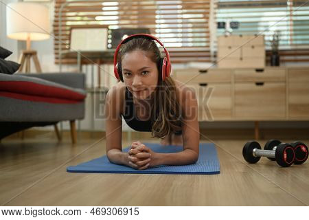 Strong Athletic Woman With Wireless Headphone Doing Plank Exercise On Matin Living Room