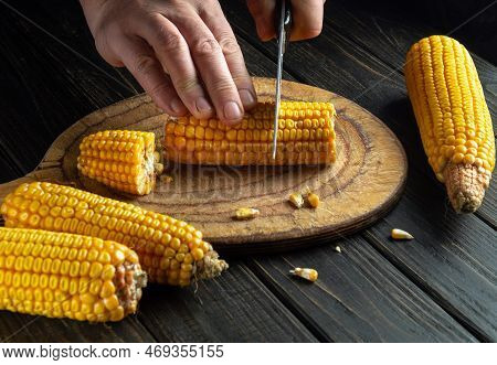 Cook's Hands With A Knife Cut Corn Kernels On A Cutting Kitchen Board. Maize Is An Excellent Dietary