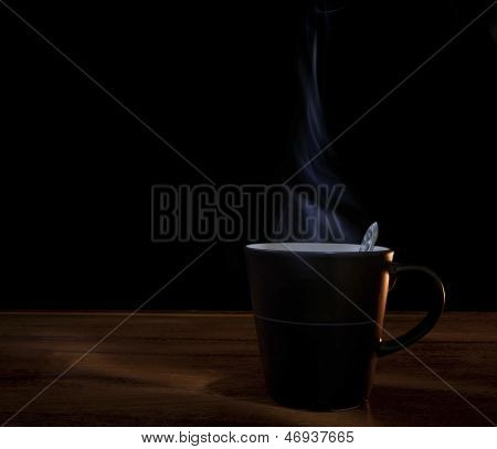 ถ้วยกาแฟร้อนบนไม้กับพื้นหลังมืดดำ