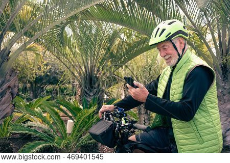 Portrait Of A Smiling Senior Man Using Smart Phone While Bike Ride In Outdoor Tropical Place. White-