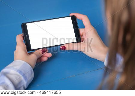 Mockup Image: Woman Looking At Black Smartphone With White Blank Screen On Blue Table. Close Up View