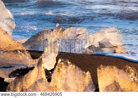 Diamond Beach In Iceland. Icebergs Shining On Black Volcanic Sand. Clear Ice Crashed By Ocean Waves.