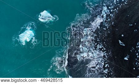 Pure Blue Glacier Ice On Black Sand Beach. Turquoise Sea Water. Icebergs At Diamond Beach In Iceland