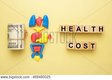 Flatlay Picture Of Fake Cash, Toy Organ And Wooden Block Written Health Cost.