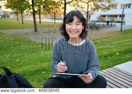 Young Girl, Korean Artist Or Art Student Sits In Park With Digital Tablet, Draws With Graphic Pen, S
