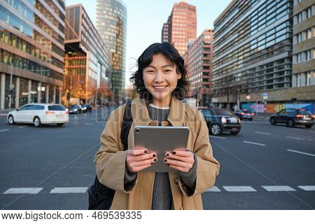 Portrait Of Asian Girl Student, Stands In City Centre With Cars On Busy Street, Holds Digital Tablet