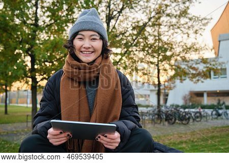 Portrait Of Asian Girl Relaxing In Park, Watching Videos Or Reading On Digital Tablet, Sitting On Be