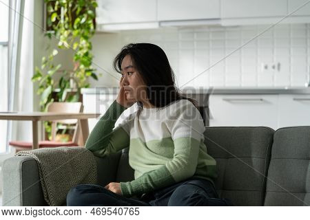 Anxious Asian Millennial Girl Sitting On Sofa Feeling Lonely, Suffering From Monophobia. Sad Depress