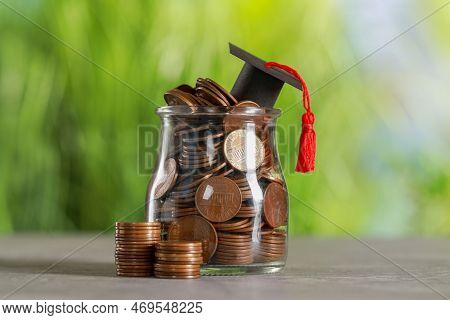 Scholarship Concept. Graduation Cap And Jar With Coins On Grey Table Against Blurred Background