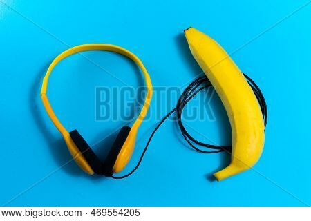 Minimalism Flat Lay Concept, Listens To Music. Headphones, Banana On Blue Background. Top View
