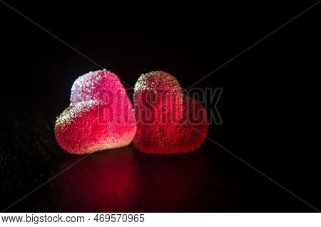 Two Red Sugar Marmalade Candies In Shape Of A Heart On A Black Background, Lit From The Side, With C