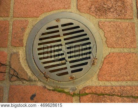 A Weathered Storn Drain With Bars Pattern And Broken Bricks Patio