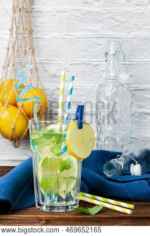 Lemonade With Mint In Glass, Lemons In Grid Bag And Bottles On Wooden Table. Side View Of Fresh Citr