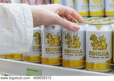 Man Picks Up A Can Of Popular Thai Beer Singha From A Supermarket Shelf. Brand Singha Beer On A Shel