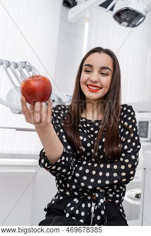 Girl Standing In Stomatology With Apple In Hands. Modern Dental Tools On Blurred Background. Healthy