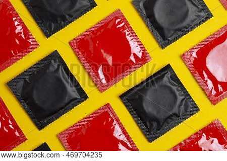 Red And Black Condoms On Yellow Background, Safe Sex Concept