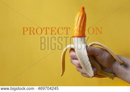 Hand Holds A Banana With A Condom, A Contraceptive Dressed On A Sexualized Banana On A Yellow Backgr