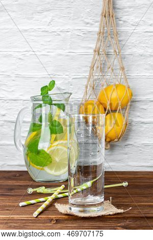 Lemonade With Mint In Jug, Glass And Lemons In Grid Bag On Wooden Table. Side View Of Fresh Citrus.
